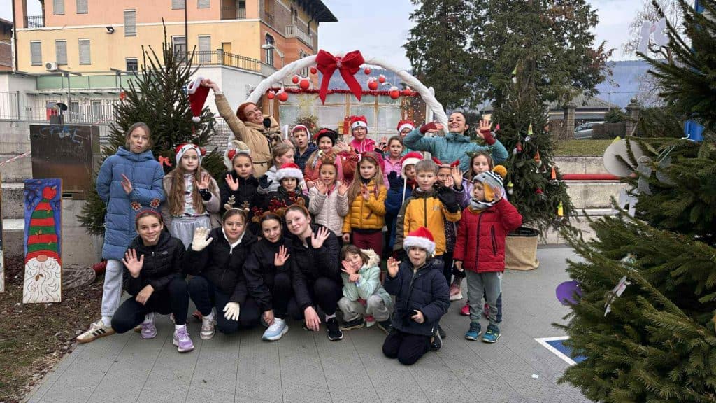 v ospredju skupina otrok z odraslo osebo, praznično okrašeni zimski motivi in drevesa.