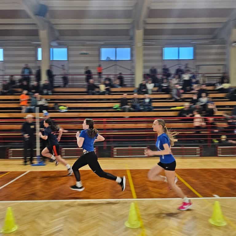 Dekleta tekmujejo v notranji atletski disciplini v dvorani.