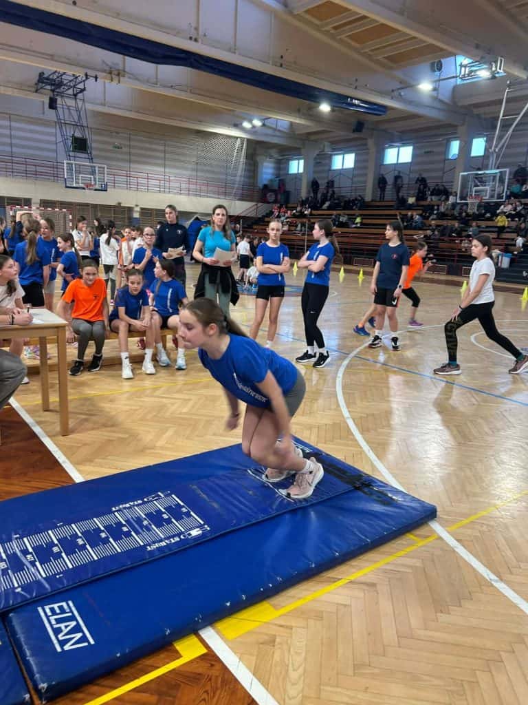 Otroci in mladostniki na tekmovanju v skoku v daljino v dvorani.